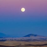 Purple and Blue sky with a Harvest Moon over a mountain landscape