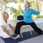 Female teacher instructing an elderly woman in a gentle standing yoga pose