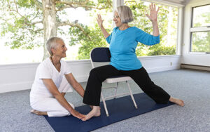 Female teacher instructing an elderly woman in a gentle standing yoga pose