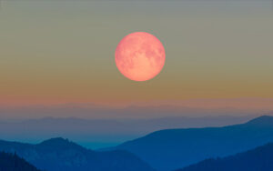 Pink moon rising over blue mountains