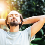 Man with hands behind his head soaking up the sunlight streaming through the trees