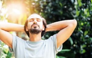 Man with hands behind his head soaking up the sunlight streaming through the trees