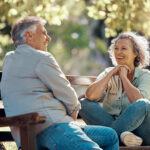 Older couple sitting on a park bend in joyful conversation