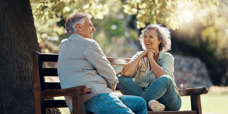 Older couple sitting on a park bend in joyful conversation